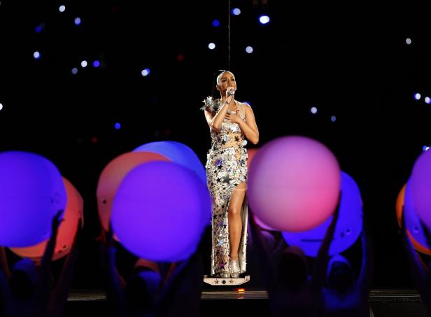 Katy Perry tritt in einem glitzernden, sternförmigen Kleid auf einer Bühne auf.