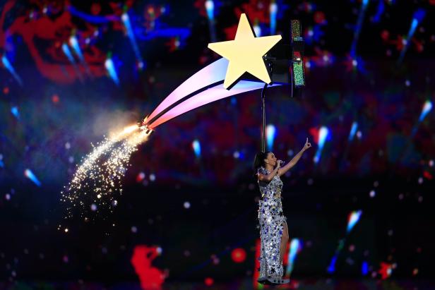 Katy Perry schwebt an einem Stern hängend über der Bühne, während Funken sprühen.