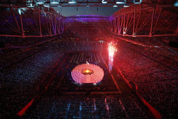 Blick von oben auf ein beleuchtetes Stadion mit einer Bühnenshow und Feuerwerk.