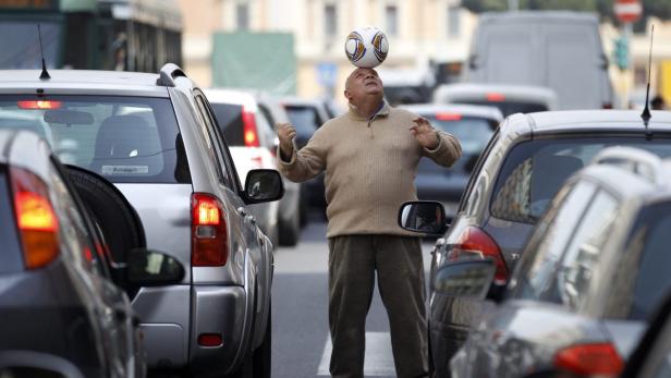 Ein Mann balanciert einen Fußball auf dem Kopf inmitten eines Staus.