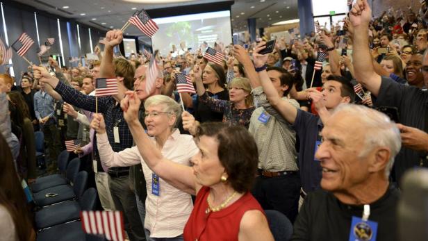 Eine Menschenmenge schwenkt amerikanische Flaggen in einem Saal.