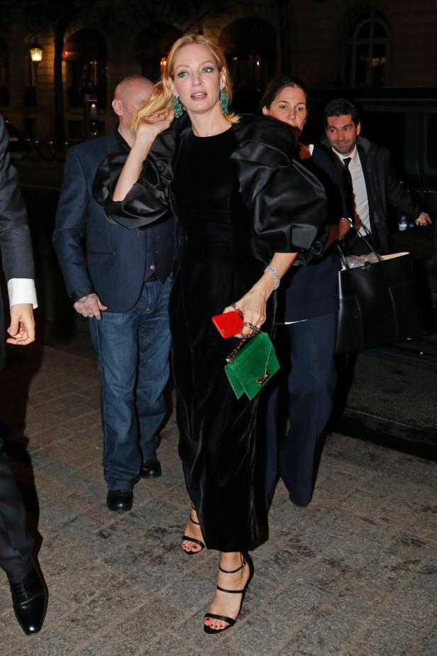 Uma Thurman in einem schwarzen Kleid mit Puffärmeln und grüner Handtasche.