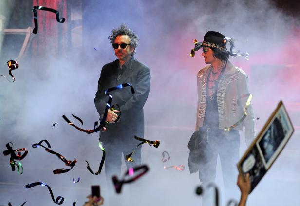 Tim Burton und Johnny Depp stehen auf einer Bühne inmitten von Konfetti und Nebel.