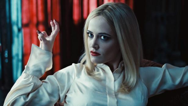Eva Green in einem hellen Seidenhemd mit rotem Lippenstift und hochgesteckter Hand.