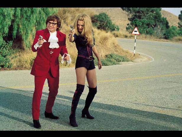 Austin Powers und eine Frau zielen mit Pistolen auf einer Straße.