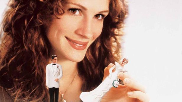 Julia Roberts hält eine Tortenfigur in Brautkleid in der Hand.