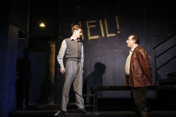 Zwei Männer stehen vor einer Wand mit der Aufschrift „HEIL!“.