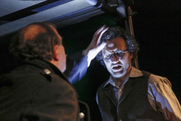 Ein Mann mit Brille wird von einer anderen Person berührt, während er den Mund öffnet.