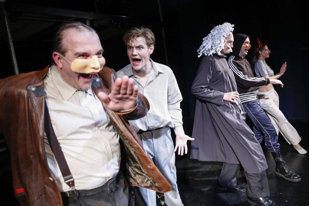 Mehrere Schauspieler stehen auf einer Bühne, einige tragen Masken und Kostüme.