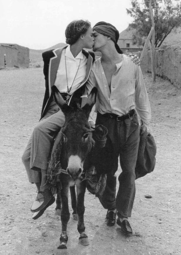 Zwei Menschen küssen sich auf einem Esel in einer staubigen Landschaft.