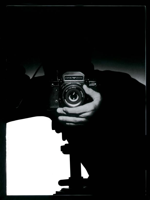 Eine Hand hält eine analoge Emporio Armani Kamera auf einem Stativ.