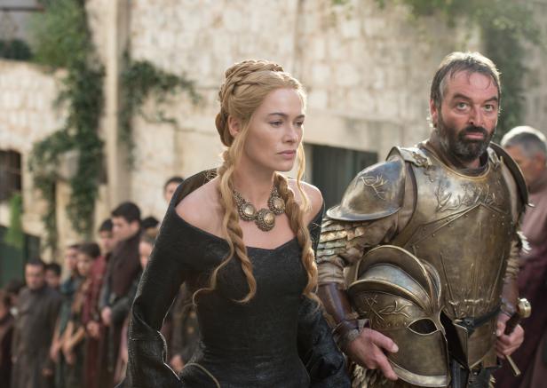 Cersei Lannister in einem schwarzen Kleid mit einem Leibwächter in Rüstung.