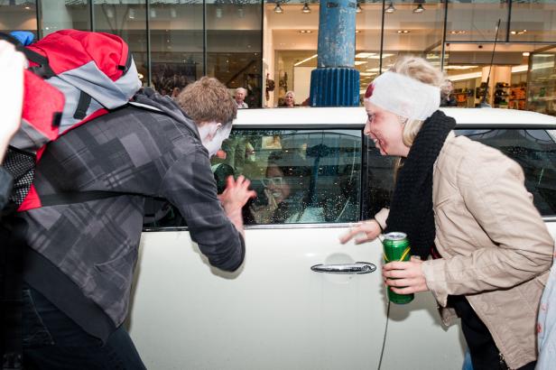 Zwei als Zombies verkleidete Personen greifen ein Auto an, in dem eine Frau sitzt.