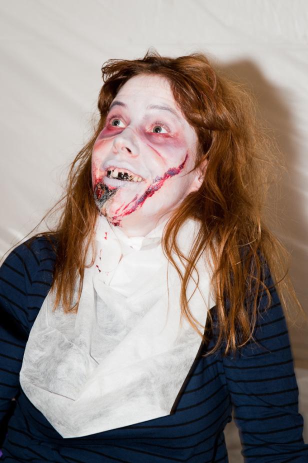 Eine Frau mit Zombie-Make-up und blutverschmiertem Gesicht blickt nach oben.
