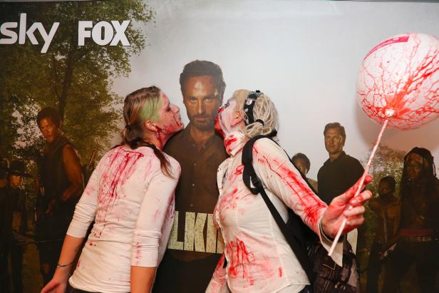 Zwei als Zombies verkleidete Frauen posieren vor einem „The Walking Dead“-Poster.