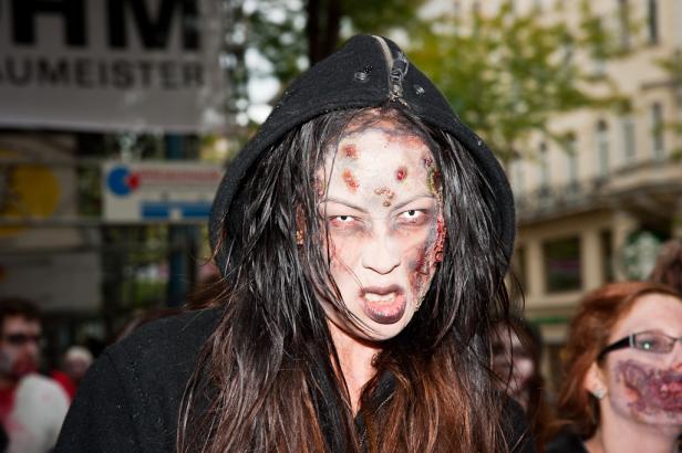 Eine Frau mit Zombie-Make-up und Kapuze blickt die Kamera an.