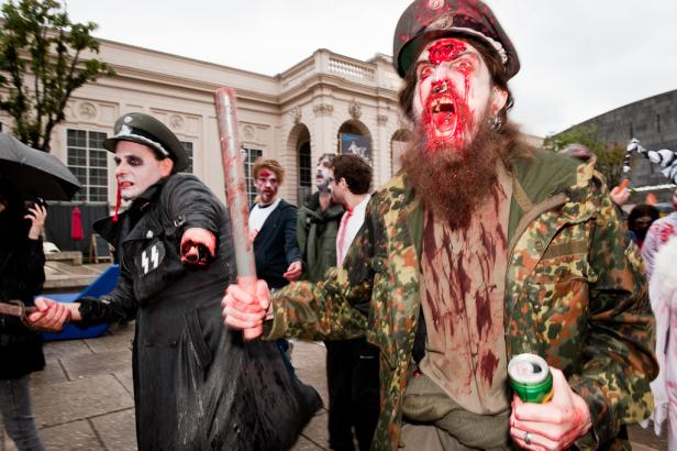Mehrere als blutige Zombies verkleidete Menschen nehmen an einer Parade teil.
