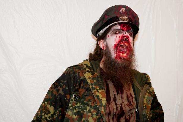 Ein als Zombie verkleideter Mann mit Bart und Militärmütze schreit.