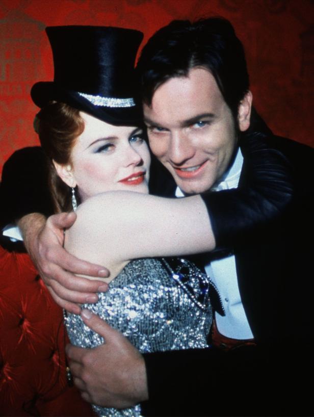 Nicole Kidman und Ewan McGregor umarmen sich auf einem roten Sofa.