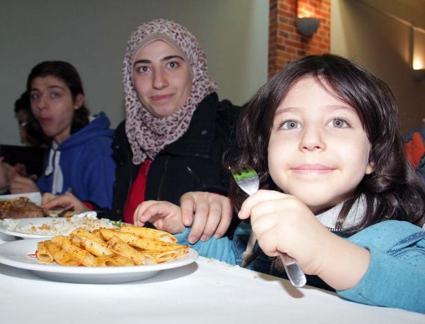 Eine Gruppe von Menschen sitzt an einem Tisch mit Pasta und anderen Speisen.