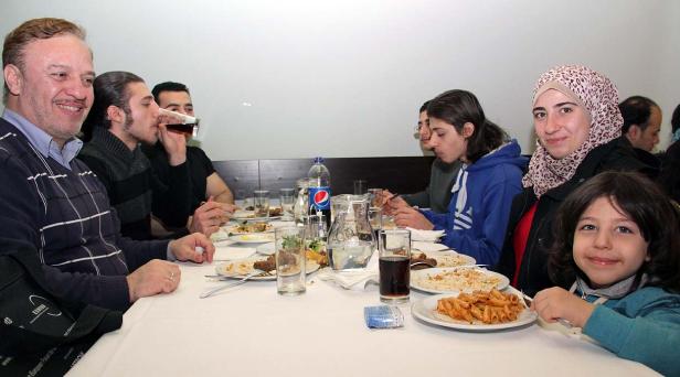 Eine Gruppe von Menschen sitzt an einem Tisch und isst Pasta und andere Speisen.