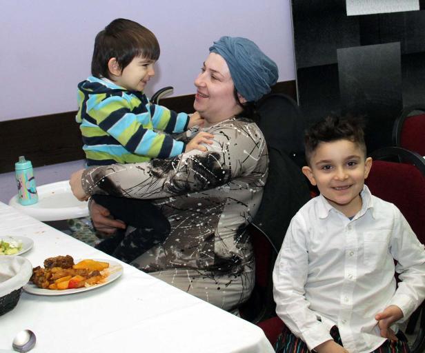 Eine Frau mit Kopftuch hält ein Kind, während ein anderes Kind daneben sitzt.