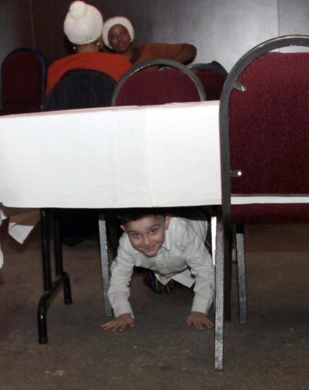 Ein Junge krabbelt unter einem Tisch mit weißer Tischdecke.