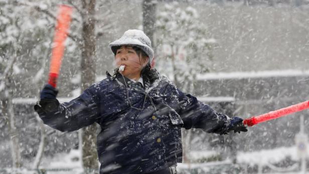 Eine Frau mit Trillerpfeife und Leuchtstäben regelt den Verkehr im Schneefall.