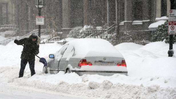 Eine Person schaufelt Schnee von einem Auto während eines starken Schneefalls.