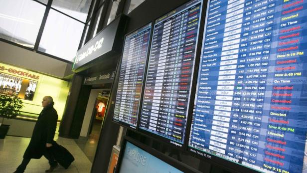 Ein Mann zieht einen Koffer an einer Anzeigetafel mit Flugdaten auf einem Flughafen vorbei.