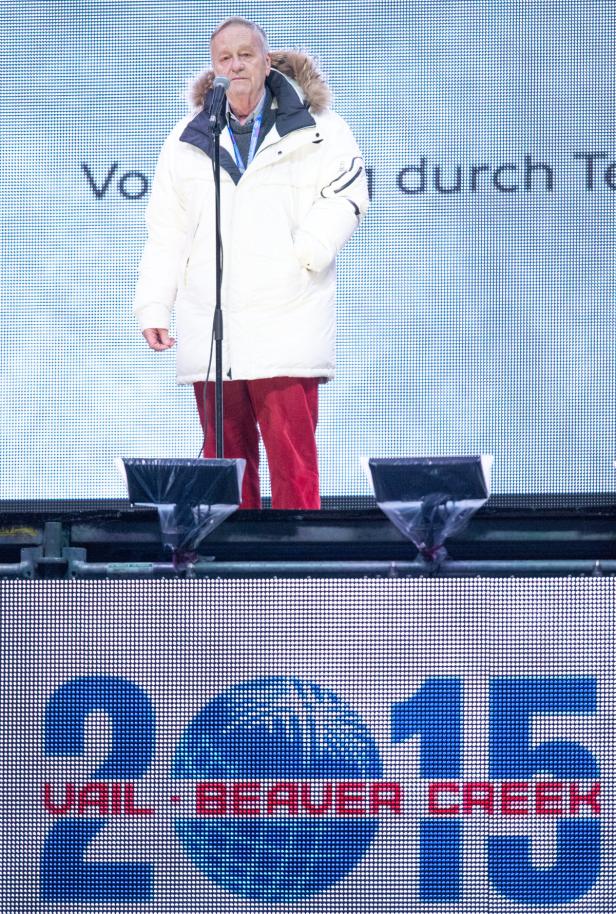 Ein Mann in Winterkleidung steht auf einer Bühne vor einer LED-Wand.