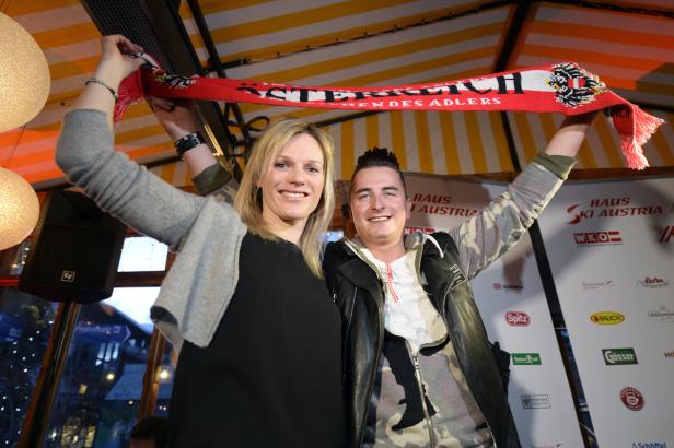 Eine Frau und ein Mann halten einen Fanschal des österreichischen Skiverbandes hoch.