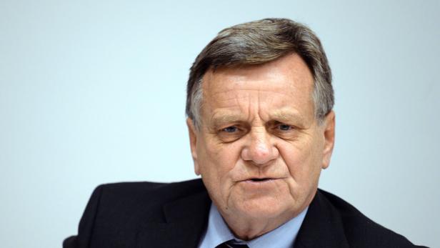 Porträt eines älteren Mannes in Anzug und Krawatte vor einem hellen Hintergrund.