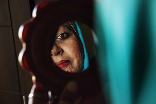 Eine Frau mit Kopftuch blickt in einen Handspiegel.