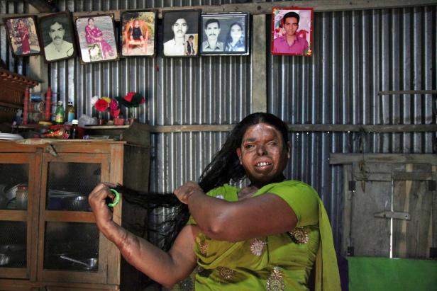 Eine Frau in einem grünen Sari kämmt sich die Haare in einem einfachen Haus.