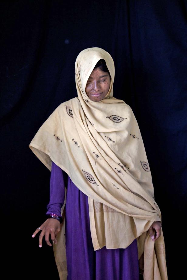 Eine Frau mit Kopftuch und lila Kleid vor einem schwarzen Hintergrund.