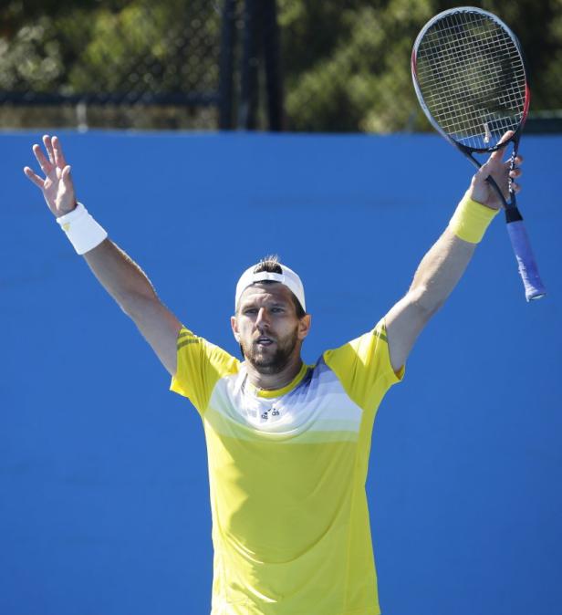 Ein Tennisspieler mit gelbem Hemd und weißer Kappe jubelt mit erhobenen Armen.