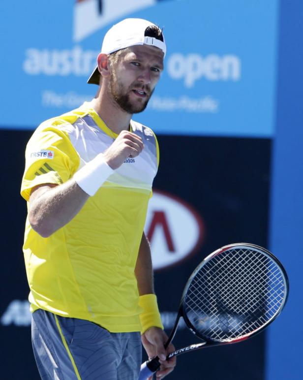 Ein Tennisspieler in gelbem Hemd und weißer Kappe ballt die Faust.