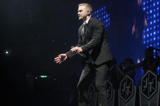 Justin Timberlake tritt in einem schwarzen Anzug auf einer Bühne auf.