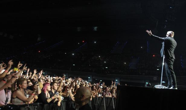 Ein Sänger steht auf einer Bühne vor einem jubelnden Publikum.