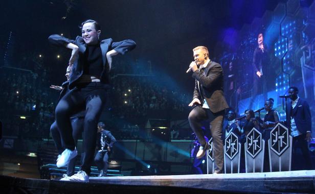 Justin Timberlake tritt mit Tänzern und Band auf einer Bühne vor Publikum auf.