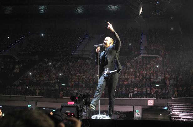 Ein Sänger steht auf einer Bühne vor einem großen Publikum und singt.