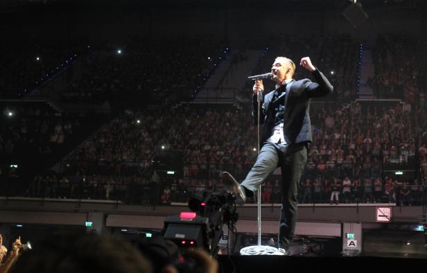 Ein Sänger steht auf der Bühne vor einem großen Publikum.