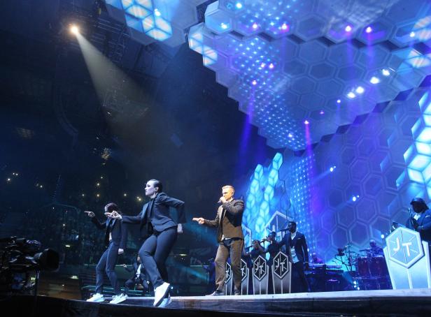 Justin Timberlake tritt mit Tänzern und Band auf einer Bühne mit blauer Beleuchtung auf.