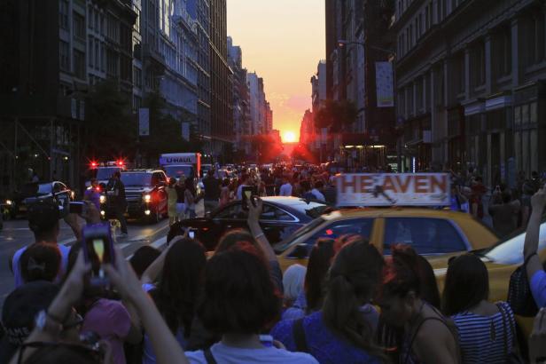 Menschen beobachten und fotografieren den Sonnenuntergang zwischen den Gebäuden einer New Yorker Straße.