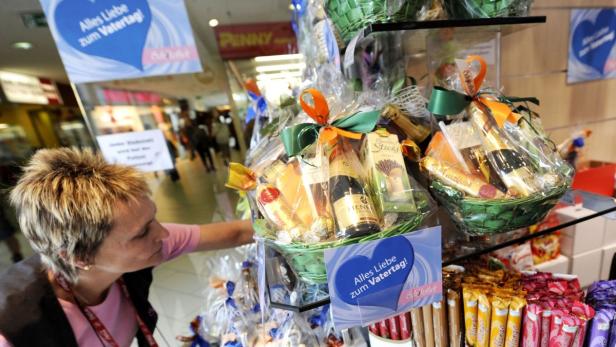 Eine Frau betrachtet Geschenk-Körbe mit Süßigkeiten und kleinen Sektflaschen zum Vatertag.