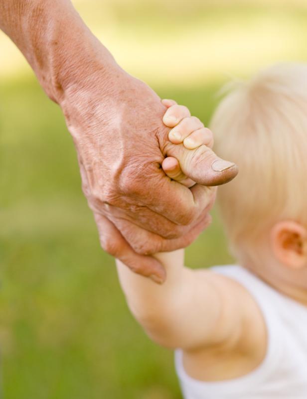 Die Hand eines älteren Menschen hält die Hand eines kleinen Kindes.