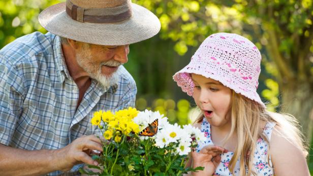 Ein Mann und ein junges Mädchen betrachten gemeinsam einen Schmetterling auf einer Blume.