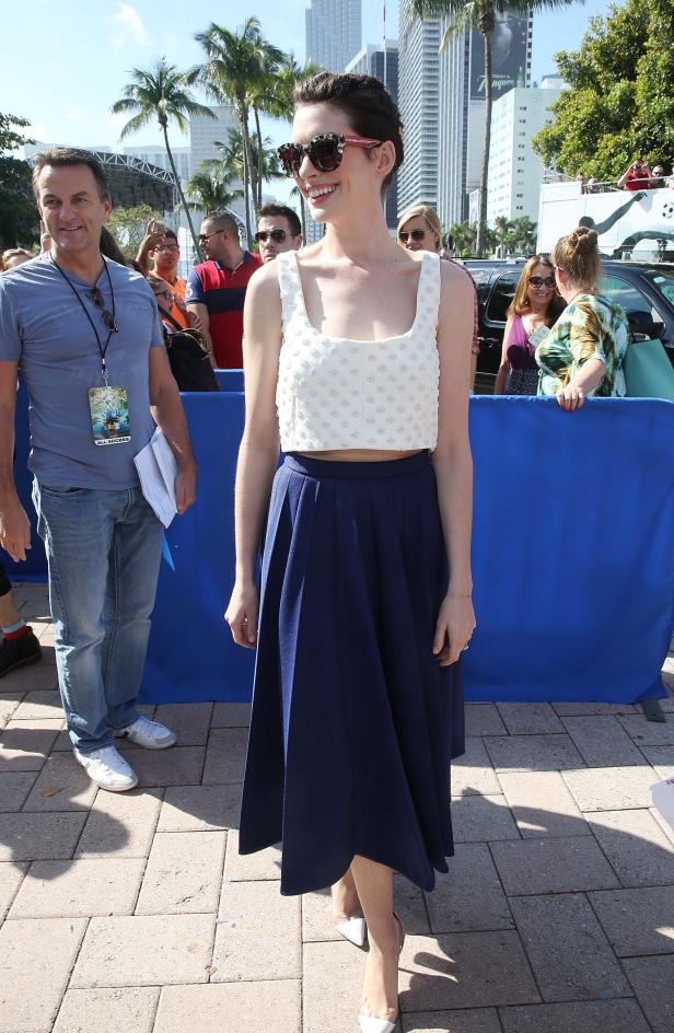 Anne Hathaway posiert in einem weißen Top und einem blauen Rock für ein Foto.