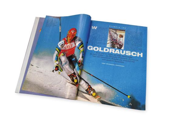 … Eine geöffnete Zeitschrift zeigt einen Skifahrer in Aktion und einen Artikel über Olympia '98 in Nagano.